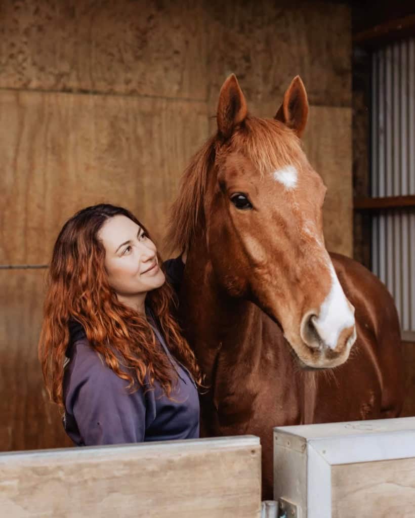 Woman with red hair and horse in stable at Reigning Downs Hauora Centre.